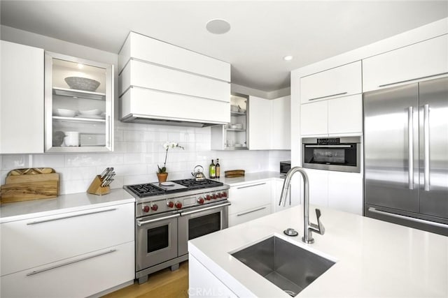 kitchen featuring modern cabinets, white cabinets, light countertops, a sink, and premium appliances
