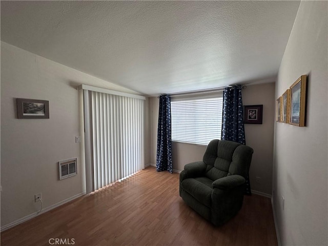 sitting room with a textured ceiling, visible vents, wood finished floors, lofted ceiling, and baseboards