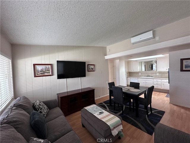 living area featuring an AC wall unit, light wood-style flooring, and a textured ceiling