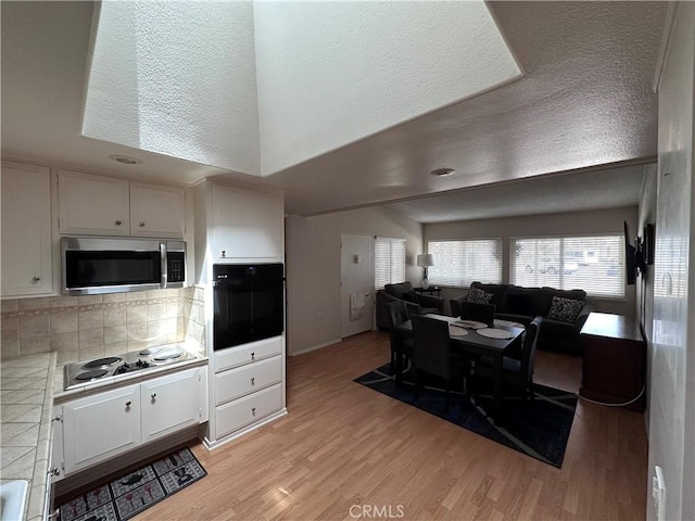 kitchen featuring oven, light wood-style floors, electric cooktop, tile counters, and stainless steel microwave