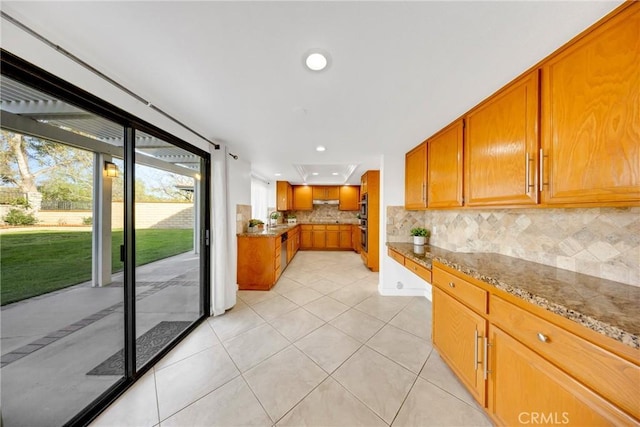kitchen featuring recessed lighting, brown cabinetry, light tile patterned floors, light stone counters, and backsplash