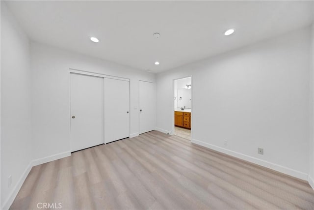 unfurnished bedroom featuring baseboards, light wood-style floors, multiple closets, and recessed lighting