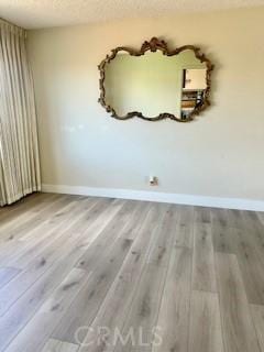 unfurnished room featuring baseboards, wood finished floors, and a textured ceiling