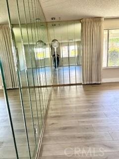 hall featuring baseboards, wood finished floors, and a textured ceiling