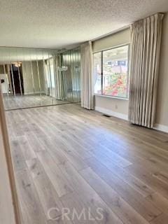 unfurnished room with visible vents, a textured ceiling, baseboards, and wood finished floors