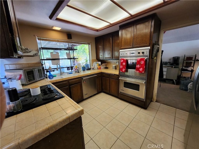 kitchen featuring dark brown cabinetry, light tile patterned floors, tile counters, and stainless steel appliances