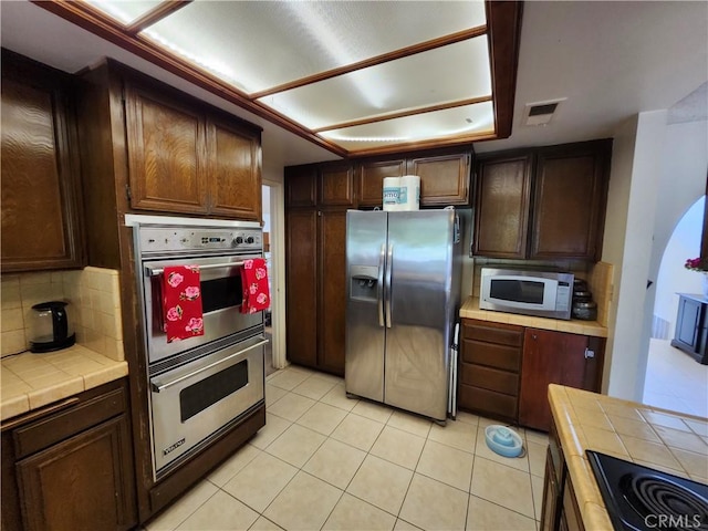kitchen with tile countertops, light tile patterned floors, visible vents, appliances with stainless steel finishes, and decorative backsplash