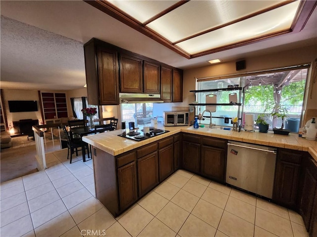 kitchen featuring a sink, under cabinet range hood, tile counters, black electric stovetop, and stainless steel dishwasher