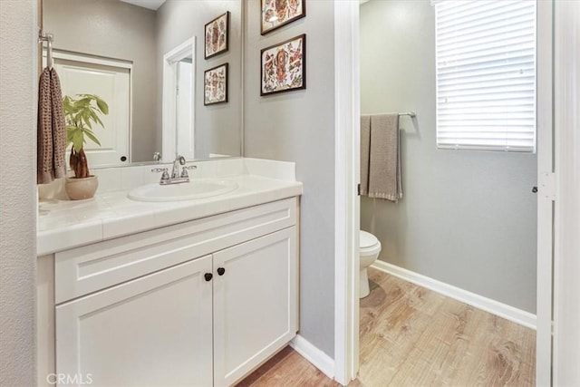 bathroom with baseboards, wood finished floors, toilet, and vanity