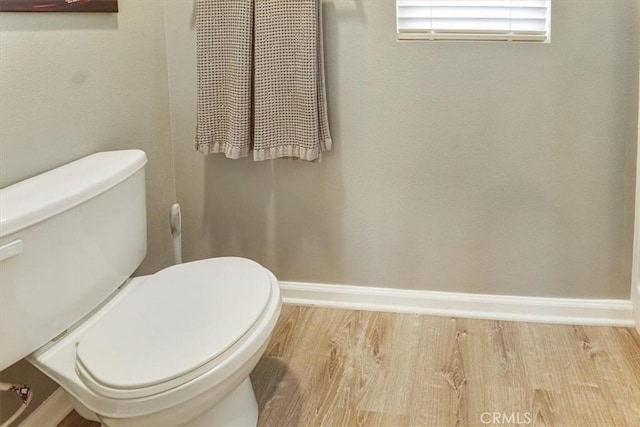 bathroom featuring baseboards, wood finished floors, and toilet