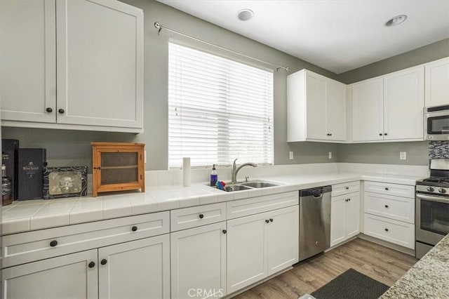 kitchen with appliances with stainless steel finishes, a sink, white cabinetry, and light wood-type flooring