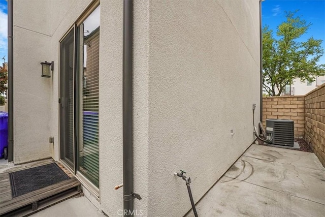 view of side of property featuring central air condition unit, fence, a patio, and stucco siding