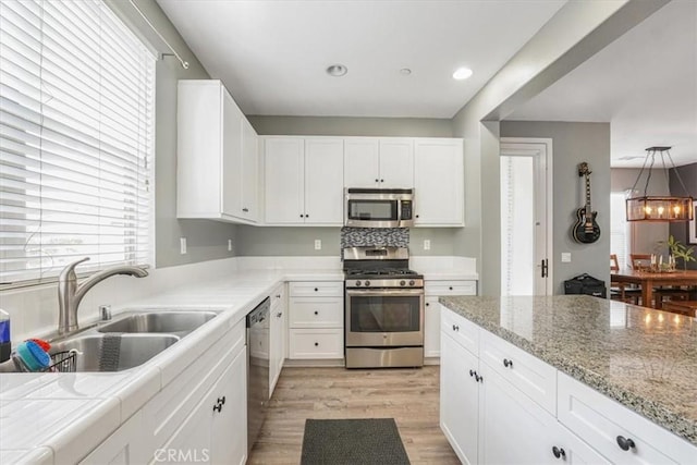 kitchen with white cabinets, stainless steel appliances, light wood finished floors, and a sink