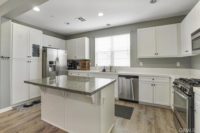 kitchen featuring white cabinets, light wood finished floors, stainless steel appliances, visible vents, and a sink