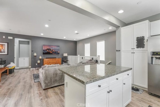 kitchen with stainless steel fridge with ice dispenser, white cabinetry, light stone countertops, and light wood-style floors