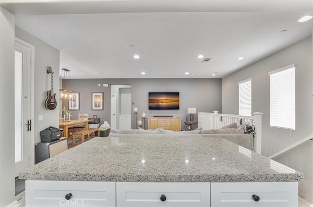kitchen with a kitchen island, light stone countertops, and white cabinetry