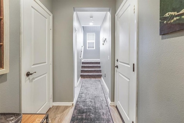 hallway with stairway, a textured wall, and wood finished floors