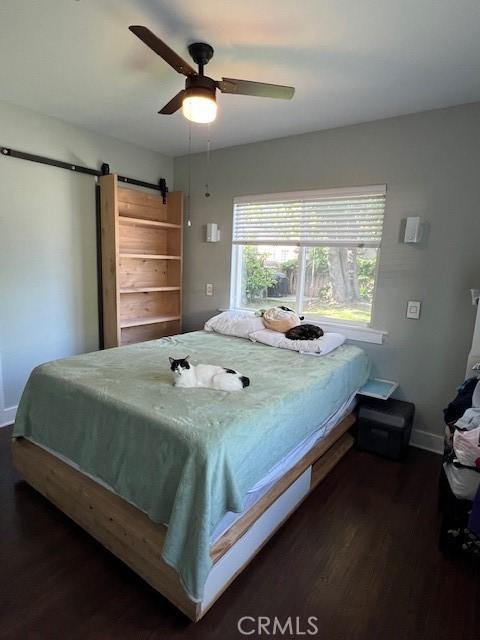 bedroom featuring a barn door, dark wood-type flooring, baseboards, and a ceiling fan