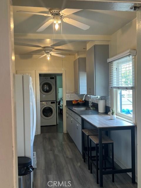 kitchen featuring a sink, ceiling fan, freestanding refrigerator, dark countertops, and stacked washer / dryer