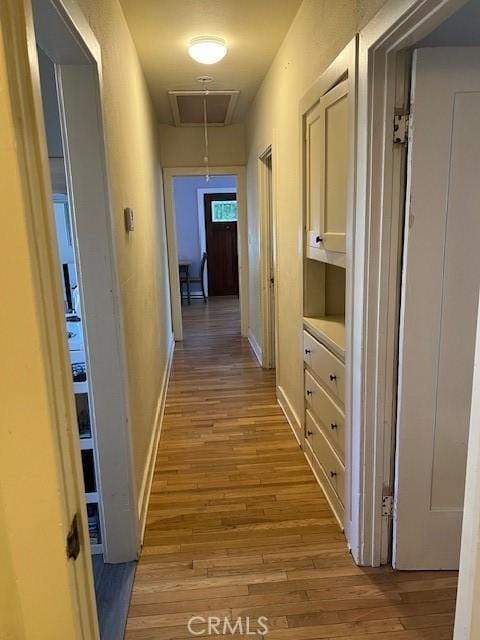 corridor with light wood-style floors, attic access, baseboards, and visible vents
