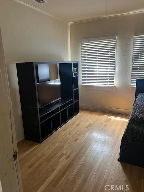 bedroom featuring ornamental molding, baseboards, light wood-type flooring, and visible vents