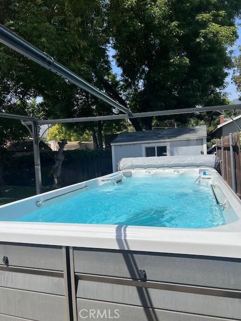 view of swimming pool featuring an outdoor structure, fence, a storage shed, and a hot tub