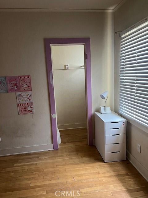 interior space with crown molding, baseboards, multiple windows, and light wood-type flooring