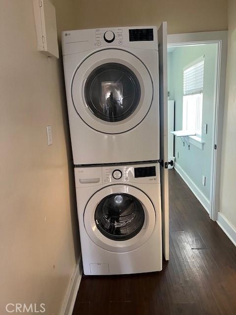 clothes washing area with dark wood finished floors, laundry area, stacked washer / drying machine, and baseboards