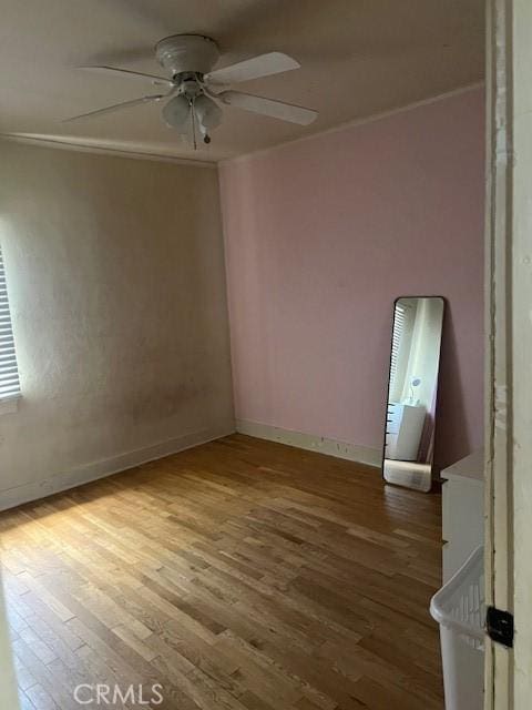 spare room featuring crown molding, baseboards, a ceiling fan, and wood finished floors