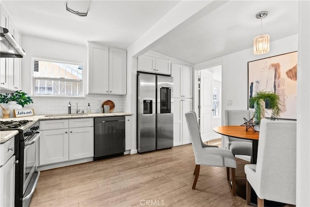 kitchen featuring light wood-type flooring, white cabinets, under cabinet range hood, stainless steel appliances, and backsplash