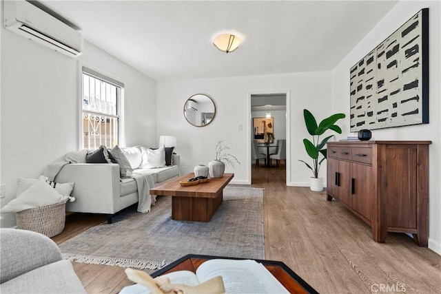 living room featuring an AC wall unit, baseboards, and light wood-style floors