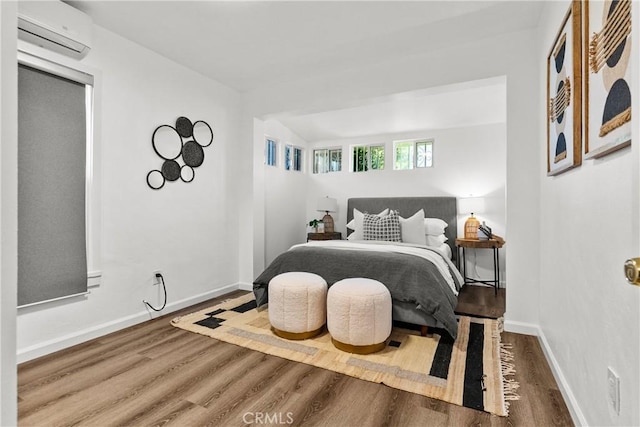 bedroom featuring wood finished floors, baseboards, an AC wall unit, and lofted ceiling