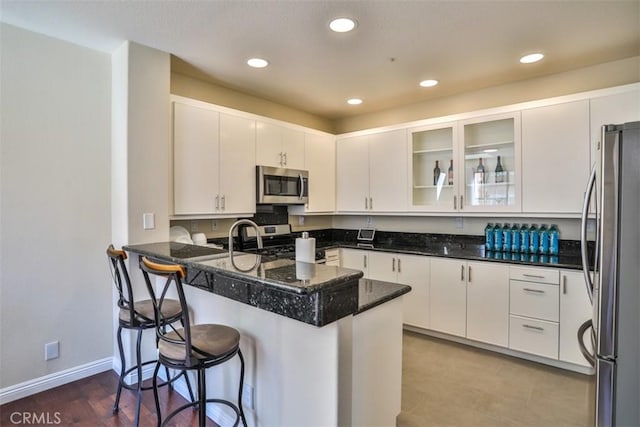kitchen featuring a peninsula, glass insert cabinets, a breakfast bar area, white cabinets, and stainless steel appliances