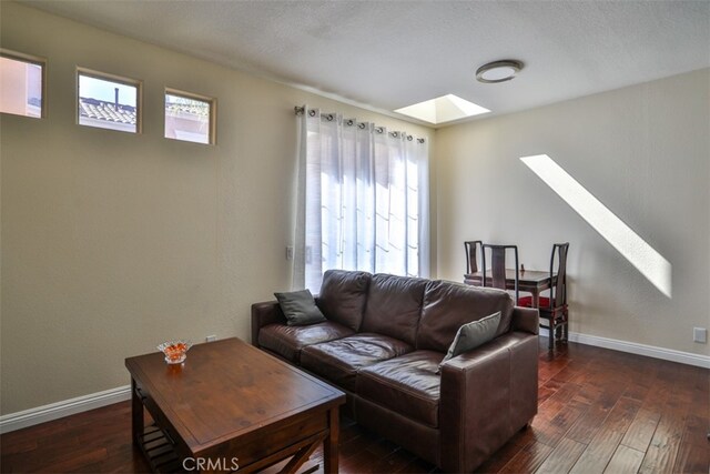living room with baseboards, a skylight, a wealth of natural light, and dark wood-type flooring
