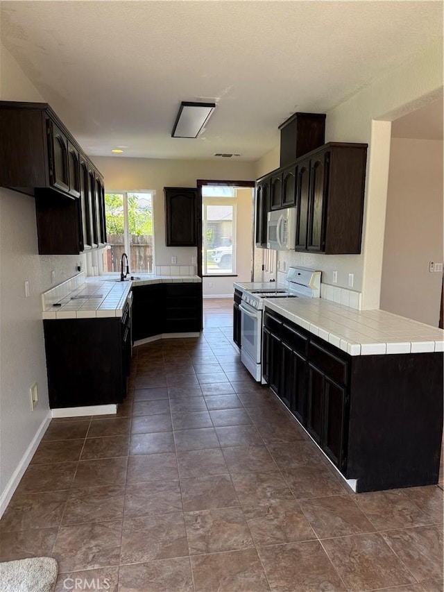 kitchen with dark brown cabinets, tile countertops, white appliances, baseboards, and tasteful backsplash