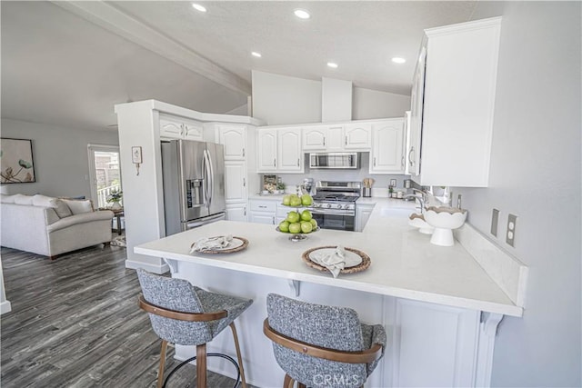 kitchen featuring a peninsula, white cabinets, dark wood-type flooring, appliances with stainless steel finishes, and vaulted ceiling with beams