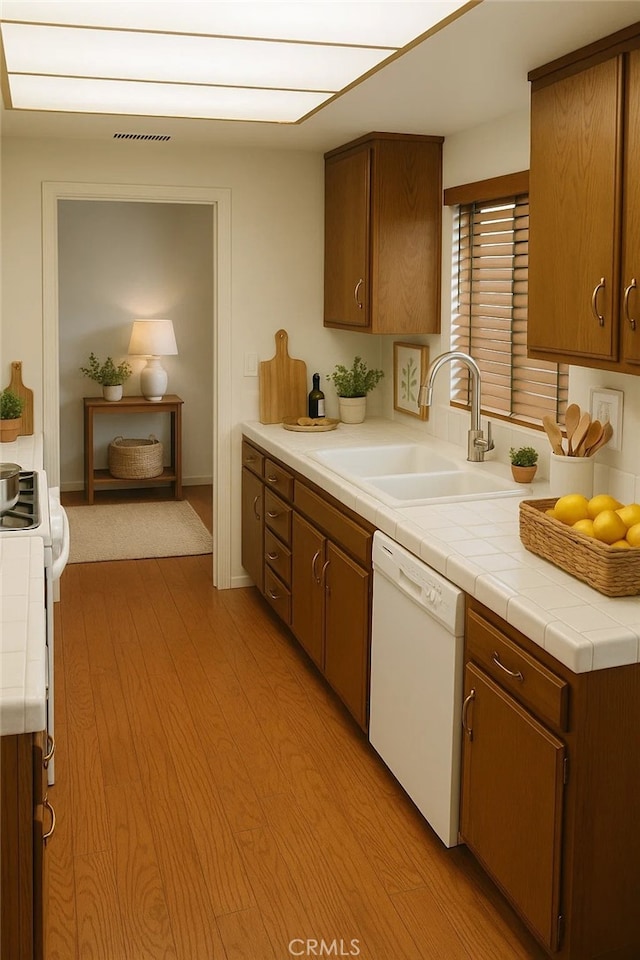 1111 S Coast Dr Unit 18, Costa Mesa, CA 92626 - kitchen with white appliances, light wood-type flooring, tile counters, and brown cabinetry