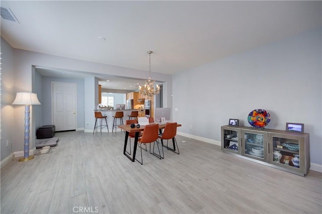 dining area featuring baseboards, light wood-style floors, a notable chandelier, and visible vents