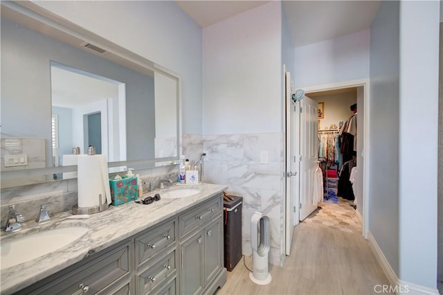 bathroom with a walk in closet, double vanity, tile walls, and a sink