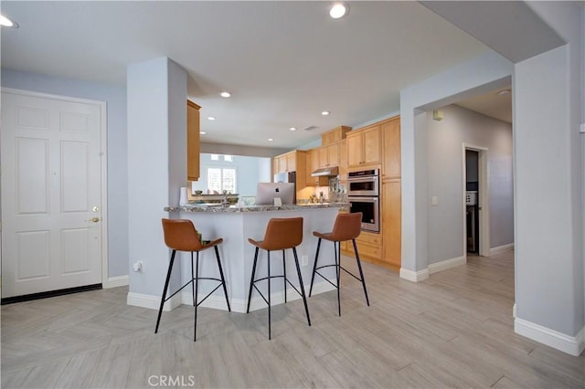 kitchen with double oven, a peninsula, recessed lighting, under cabinet range hood, and a breakfast bar area