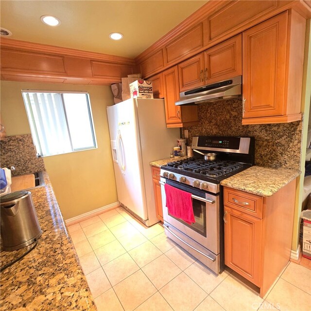 kitchen with light tile patterned flooring, white fridge with ice dispenser, stainless steel range with gas cooktop, backsplash, and under cabinet range hood