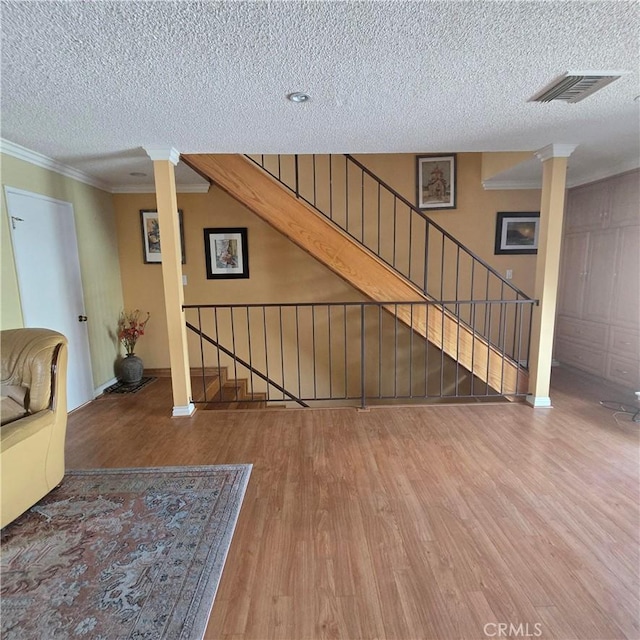 unfurnished living room featuring crown molding, a textured ceiling, decorative columns, and wood finished floors