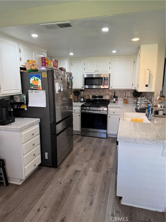 kitchen featuring visible vents, appliances with stainless steel finishes, wood finished floors, a sink, and tile counters