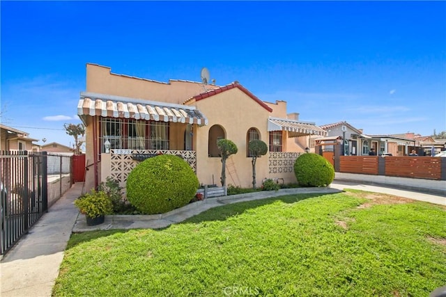 mediterranean / spanish home with a front yard, stucco siding, fence, and a tile roof