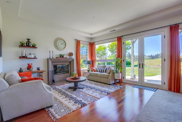 living room featuring a raised ceiling, wood finished floors, visible vents, french doors, and a glass covered fireplace