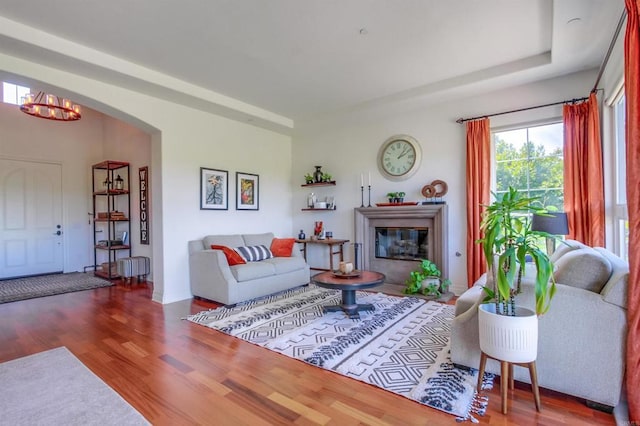 living area featuring arched walkways, a glass covered fireplace, wood finished floors, and an inviting chandelier