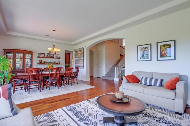 living room featuring a tray ceiling, arched walkways, a chandelier, wood finished floors, and stairway