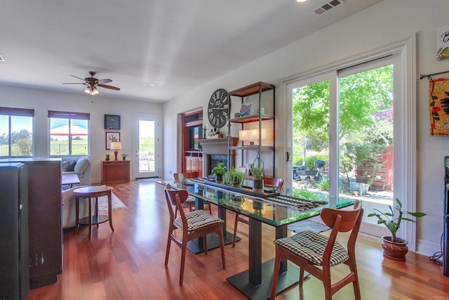 dining area featuring baseboards, visible vents, wood finished floors, ceiling fan, and a fireplace
