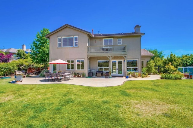 rear view of property featuring a chimney, a yard, stucco siding, french doors, and a patio