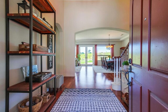 entrance foyer featuring french doors, arched walkways, an inviting chandelier, stairway, and dark wood-type flooring